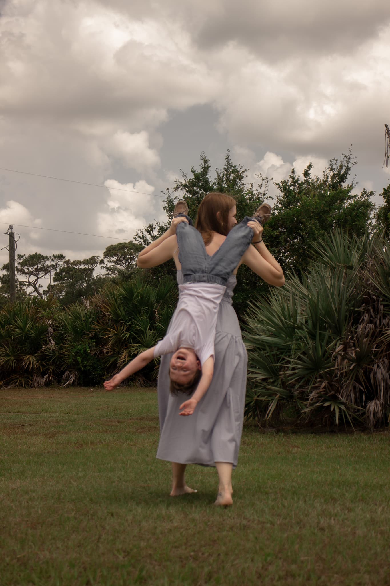 Mother playfully holding her laughing child upside down during a family session