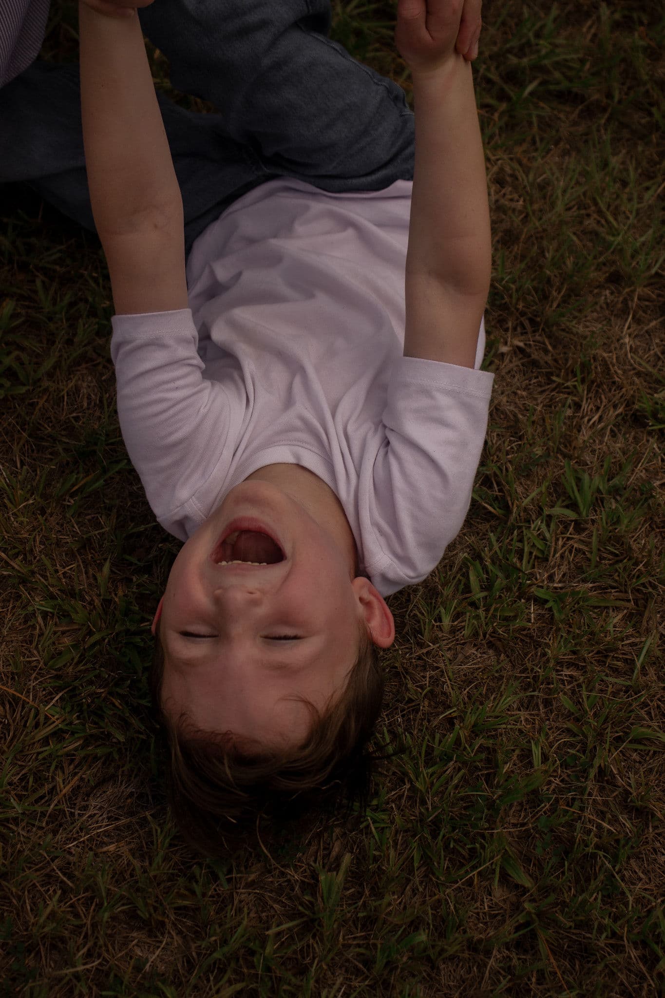 A child laughing while held upside down in the grass