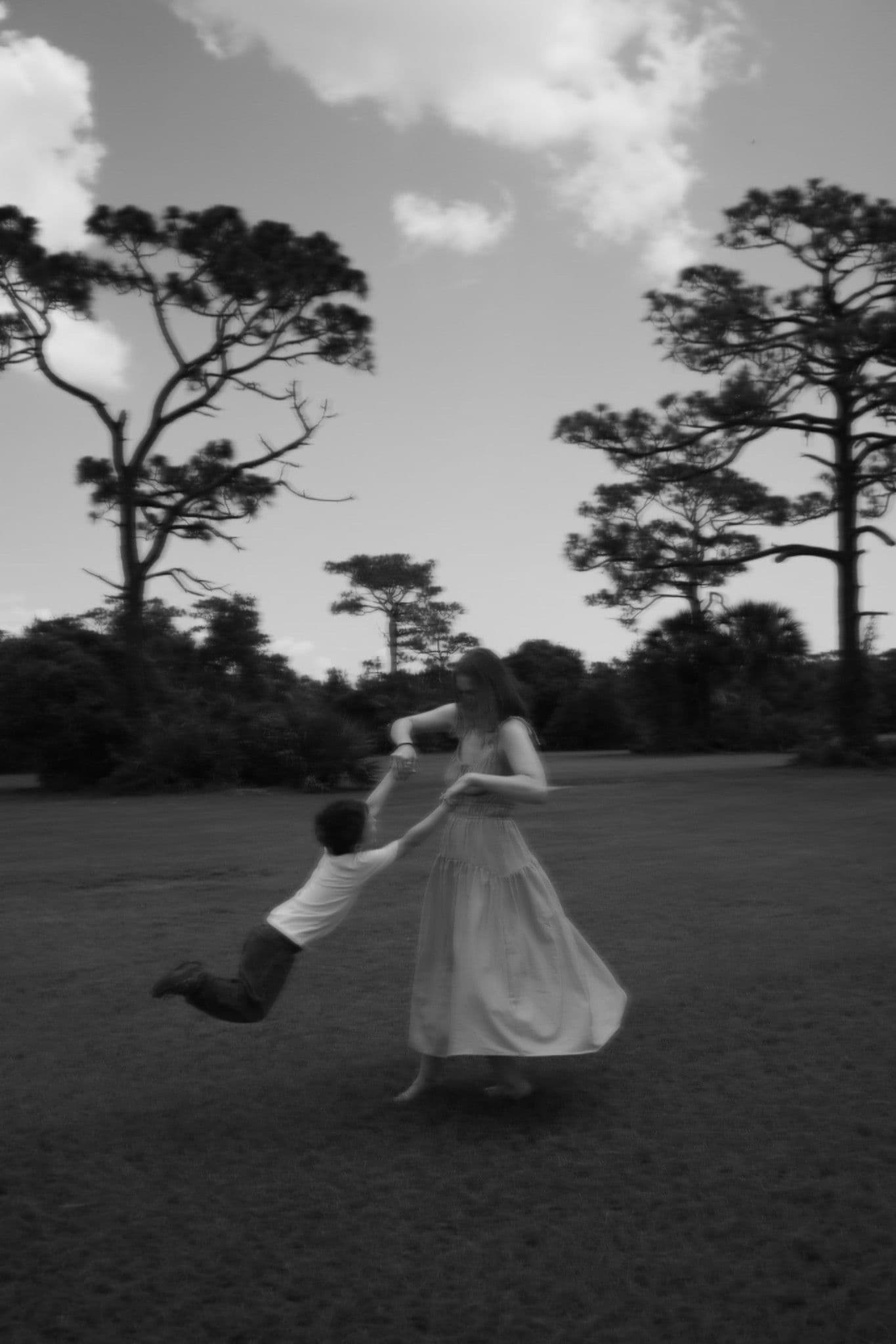 Black and white family portrait in motion beneath tall trees