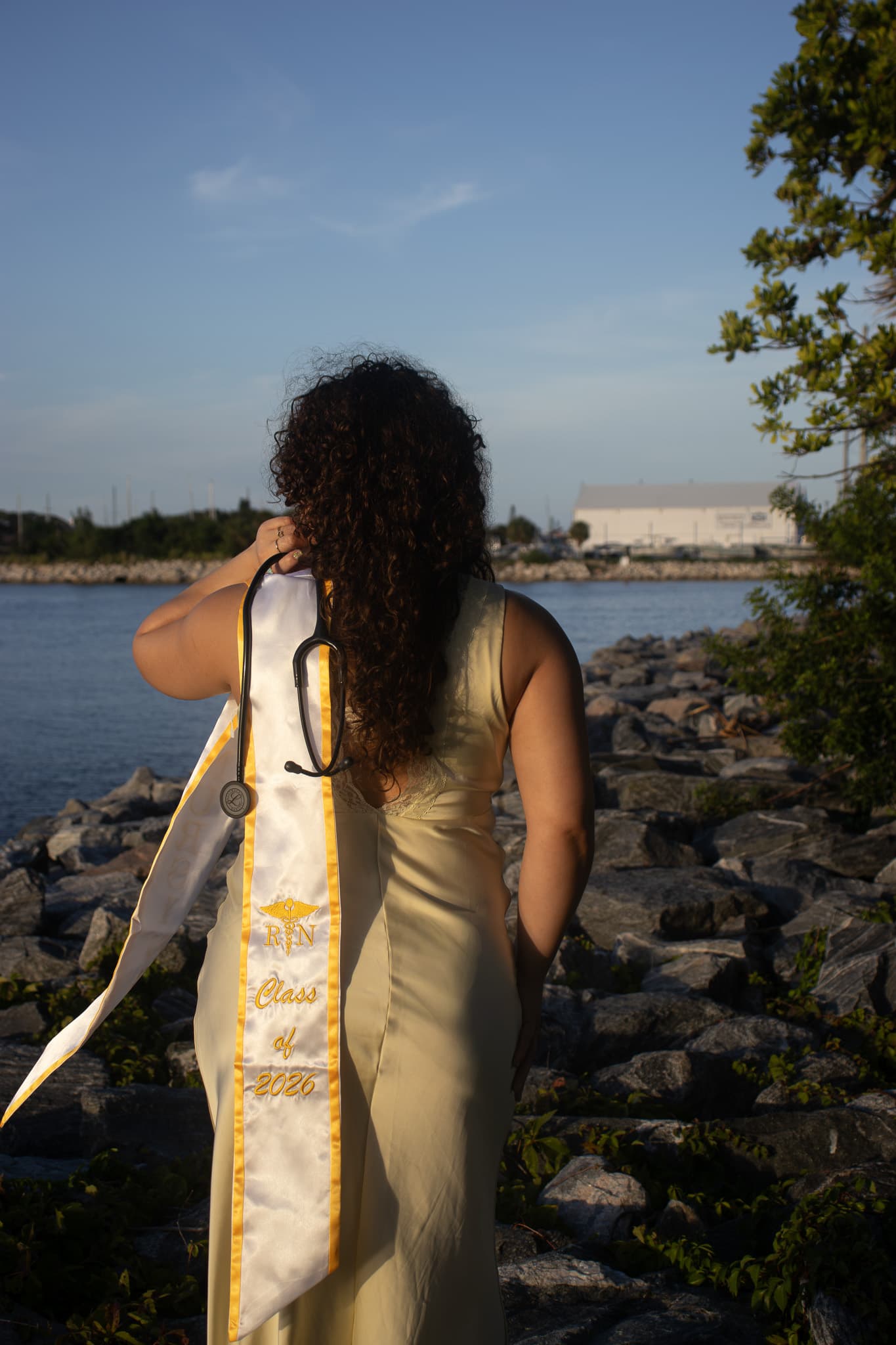 Nursing graduate wearing a Class of 2026 sash beside the water